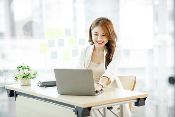 Portrait of Asian young businesswoman with laptop writes on a document at her office,Asian girl working at a office space with a laptop computer. 