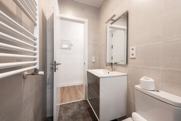 Bathroom with wooden and white furniture, white resin sink, frameless mirror, aluminum heated towel rail and gray ceramic stoneware floor