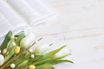 White tulips and decorative branch with easter eggs and an open bible on a white wood background with copy space