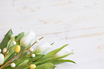 White tulips and decorative branch of easter eggs on a white wood background with copy space