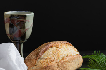 Loaf of bread and clay chalice on a black background with copy space