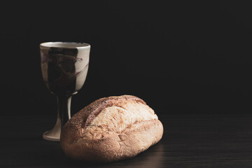 Loaf of bread and clay chalice on a black background with copy space