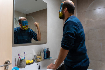 Stop war, conflict between Ukraine and Russia. The inner being in a mirror encourages him to continue fighting and enduring the invasion of a young Ukrainian with painted face in the bathroom