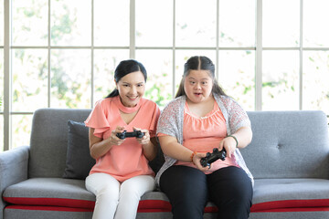 down syndrome teenage girl and mother playing game and having fun together on sofa