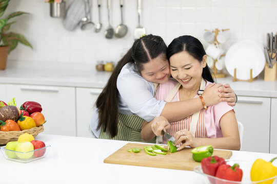 young teenage girl hugging her mother while cooking food in the kitchen