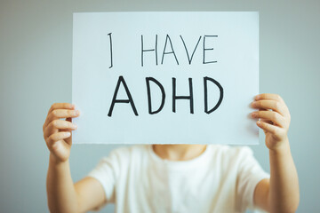 Young boy holds ADHD text written on sheet of paper. ADHD is Attention deficit hyperactivity disorder. Close up. Attention Deficit Hyperactivity Disorder or ADHD