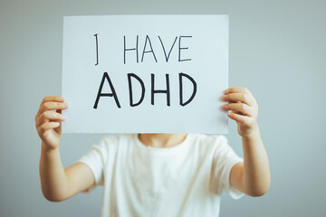 Young boy holds ADHD text written on sheet of paper. ADHD is Attention deficit hyperactivity disorder. Boy holding blackboard and admitting suffering from ADHD