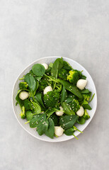 Delicious light salad with spinach, mozzarella and broccoli sprinkled with sesame seeds, top view