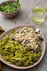 Green pasta from durum wheat and gravy with champignons fried in sour cream sauce with green onions and parsley and mozzarella, microgreens in a bowl and water with lemon