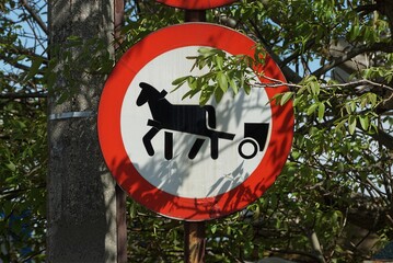 one round road sign no passage for a cart with a horse on a pole on a street in green vegetation