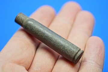 one old green copper army cartridge case lies on the fingers of the hand on a blue background