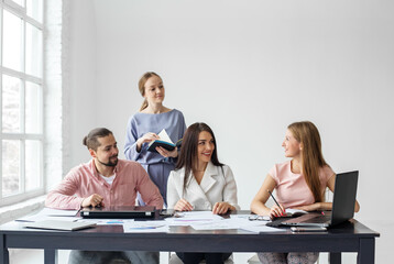 Man and three women work together in office using computers, notepads, graphs and charts.