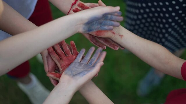 Close-up unrecognizable children stacking colorful hands in slow motion outdoors. Group of positive Caucasian boys and girls having fun painting outdoors enjoying hobby. Creativity and art concept