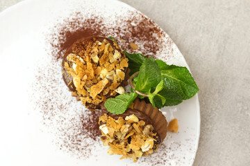 Vegan donuts topped with healthy chocolate glaze with flakes, cocoa and nuts on white plate on gray background.