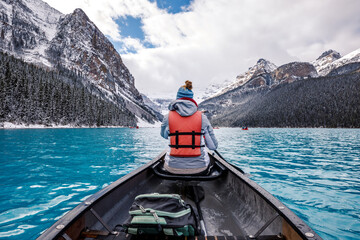 Back view of a hiker in a lifejacket in a sailboat on lake Louise in Canada - obrazy, fototapety, plakaty