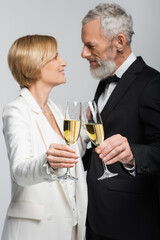 Side view of blurred mature couple in wedding clothes clinking champagne isolated on grey.