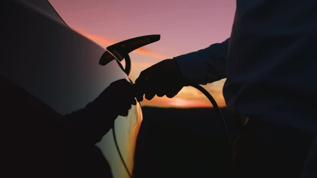 Close up male charging electric EV car outdoors at golden sun light, RED camera