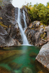Idyllic landscape in the Italian Alps with a waterfall, forests and Autumn colors and mountain in the background, Near the town of Pestarena, Piedmont, Italy - September 2021.