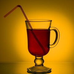 Tea, cocktail, fruit drink in a glass cup with a drinking straw on the table. Red drink in a mug on a beautiful bright yellow gradient background. Summer drinks concept