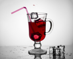 Cold tea, cocktail, fruit drink in a tall glass cup with a drinking straw on a table with pieces of ice on a white gradient background. Summer drinks concept