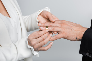 Cropped view of mature woman wearing wedding ring on groom isolated on grey.