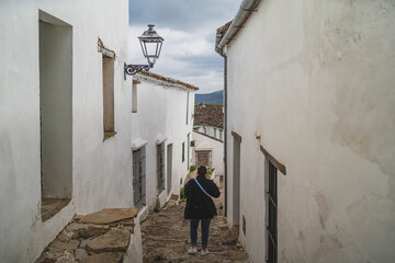 Chica joven guapa paseando por pasillos de pueblo blanco mientras sonríe y realiza fotografías