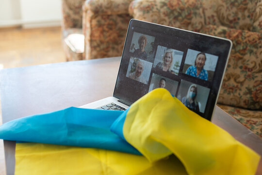 Flag of Ukraine on the background and wide digital screen of laptop with video conference. War with Russia. Cyber attack, sanctions, economic collapse. Message for world peace.