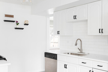 A bright kitchen with white cabinets, subway tile backsplash, black hardware, and a stainless steel...