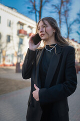 Portrait of a young beautiful girl in a business suit talking on the phone on a city street.