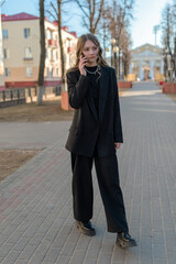 Fototapeta premium Portrait of a young beautiful girl in a business suit talking on the phone on a city street.