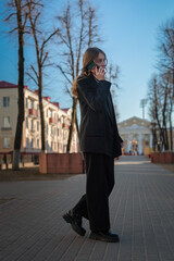 Portrait of a young beautiful girl in a business suit talking on the phone on a city street.