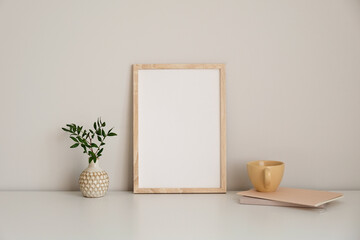Vertical picture frame mockup on white table. Vase with green branch, mug of tea, paper notebook. White wall background. Nordic style living room interior design - Powered by Adobe
