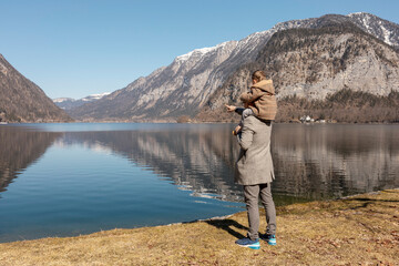 Naklejka premium Father and son enjoying mountains, snow, lake, good weather, blue sky, sun. Little boy and his father spending time together. Family time. Beautiful landscape. Tourism, holiday, travel. Amazing view.