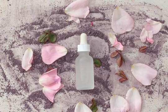 A glass white bottle with a dropper surrounded by fresh rose petals.