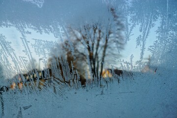 Frostmuster auf Glasscheibe vor Häuser, Bäumen und Himmel bei aufgehender Sonne am Morgen im...