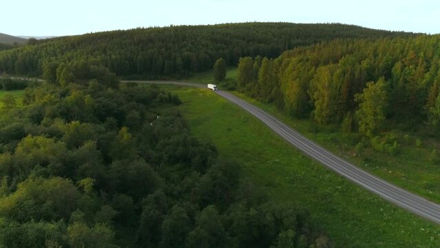  A long road with cars. The view from the drone. Scene. A bright summer landscape with seedy mountains and forest in the background next to a road with cars in summer against a bright sky.