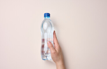 female hand holds a plastic transparent bottle on a beige background