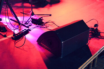 Concert stage under a red light with a lot of wires, mic stands and a big speaker on the floor