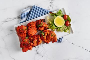 BBQ Chicken Tikka boti with lime in a dish isolated on napkin side view on grey background