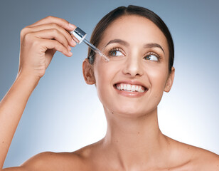 Fototapeta premium Just me on my mind. Shot of a young beautiful woman applying serum to her face against a blue background.