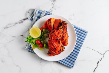 indian culture Tandoori chicken with lime in a dish isolated on napkin side view on grey background
