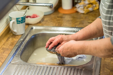 Alte Frau Oma beim Abspülen von Geschirr in einer Spüle mit Wasser und Stahlwolle in einer...
