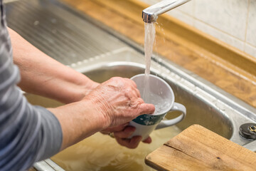 Alte Frau Oma beim Abspülen von Geschirr Kaffeetasse Tasse in einer Spüle mit laufendem Wasser...
