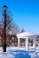 Snow-covered noble park with gazebo and lantern