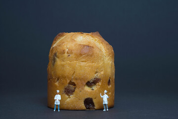 Miniature cooks with an Italian Christmas biscuit called panettone isolated on dark blue background.