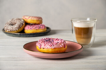 Glazed decorated donuts on plates and coffee latte or cappuccino with milk foam in a heat-resistant...