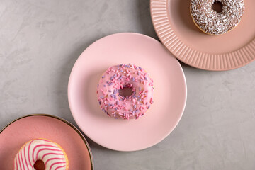 Three glazed donuts lie on tall pink plates on a gray surface. Selective focus. View from above.