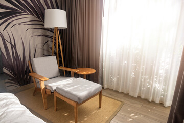 Cozy armchair to relax in living room and there is a lamp in back by window, there is a white light curtain