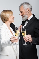 Side view of happy mature woman holding glass of champagne near groom isolated on grey.