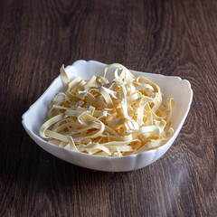 Raw pasta is on the table in a plate. On a brown background.